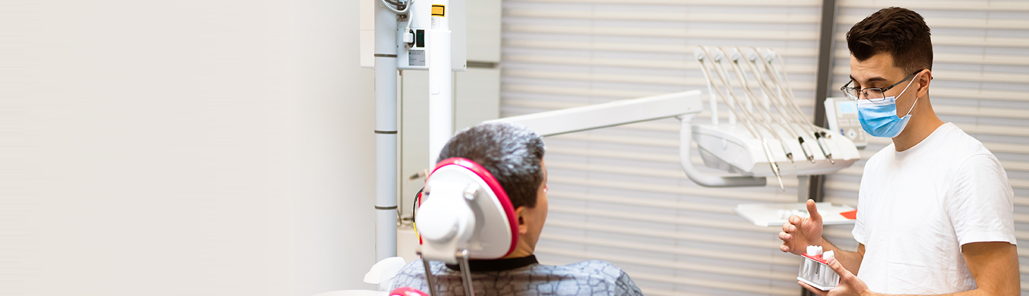 A dentist discusses treatment with a patient in a dental chair.