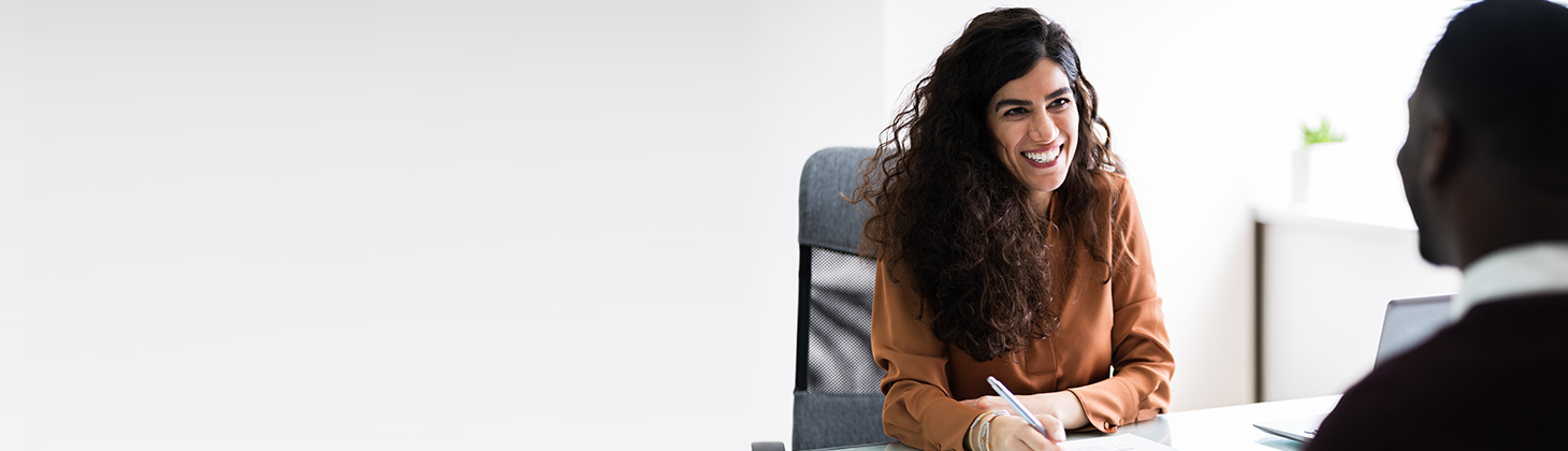 A woman with curly hair smiles at a staff member sitting across the table.